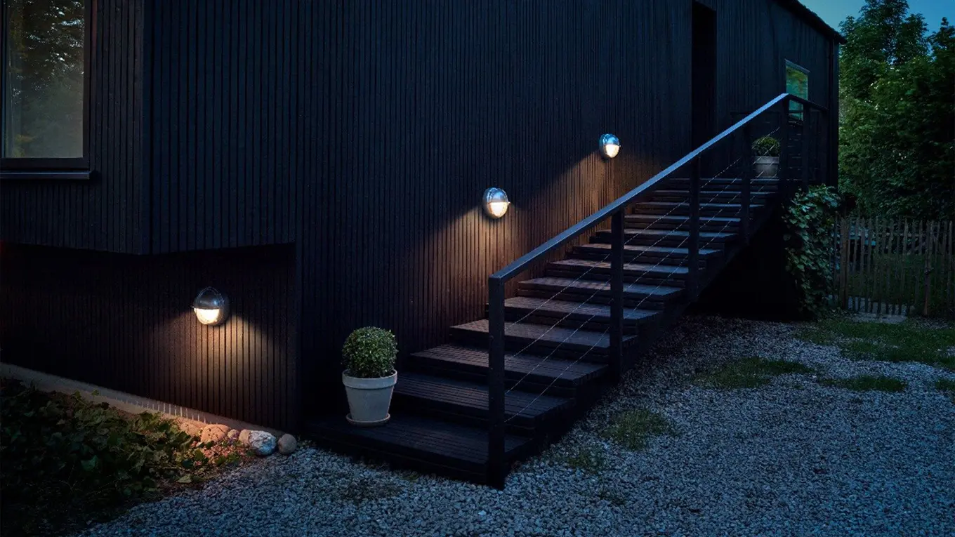 Drei Louis Poulsen Skot Außenwandleuchten an einer dunklen hauswand mit treppe