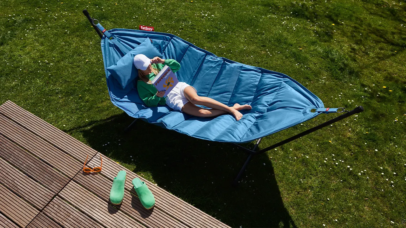 frau liegt auf einer blauen fatboy hängematte mit gestell auf einem rasen