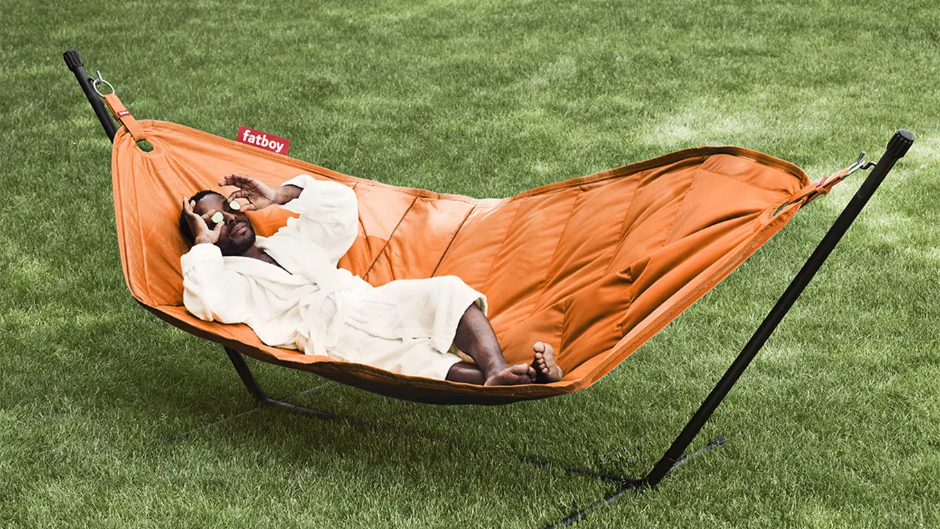 mann liegt im bademantel auf einer orangenen fatboy hängematte auf einem rasen