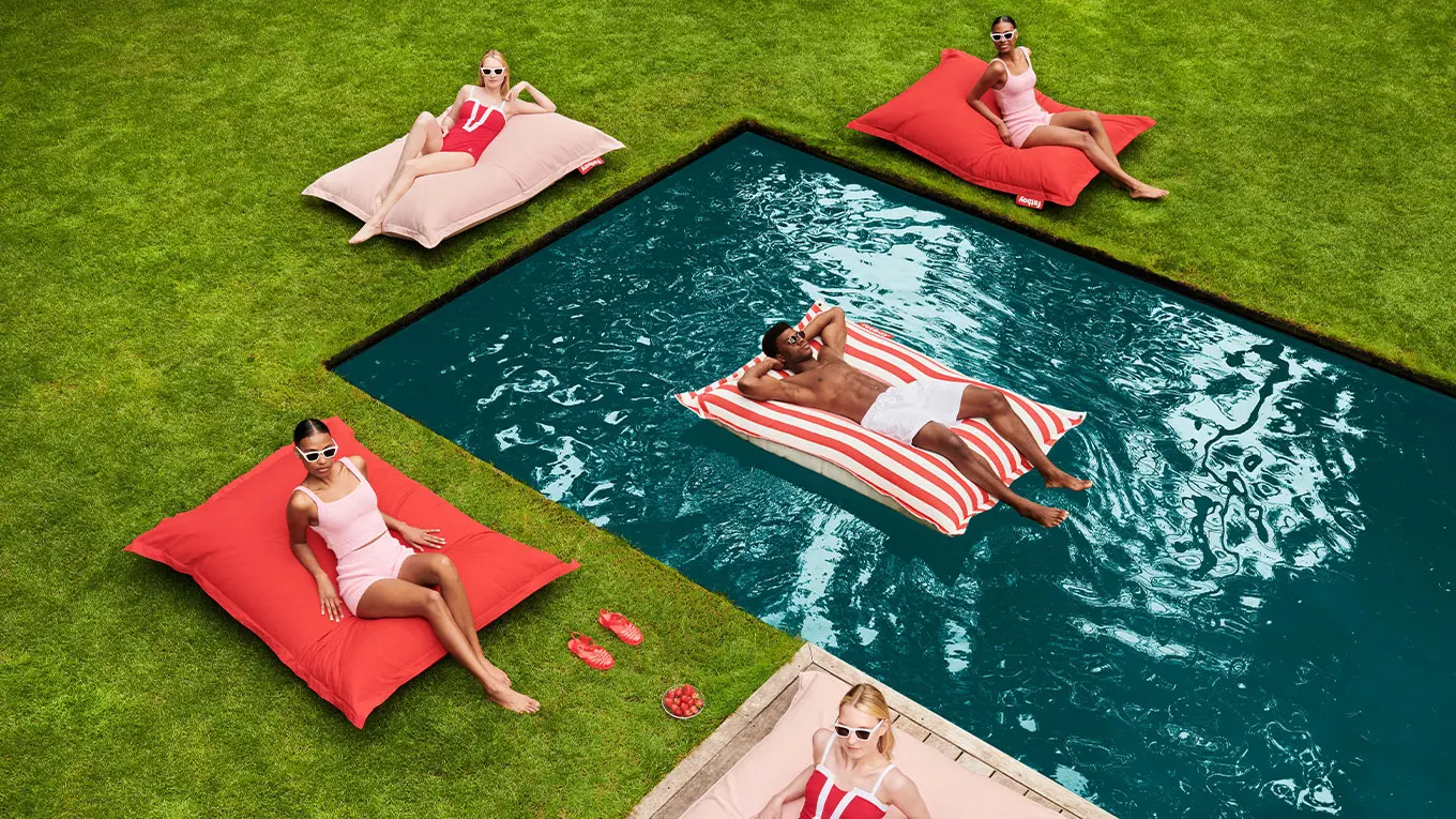 frauen und ein mann  liegen auf roten fatboy outdoor sitzsack am und im pool
